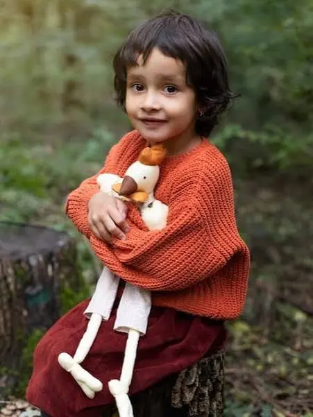 A child in an orange knitted jumper holding a soft toy, outdoors.