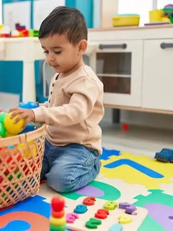 A small child kneeling beside a basket of coloured balls in a playroom.