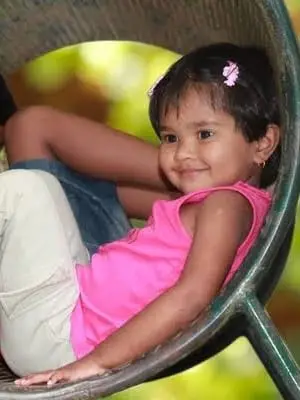 A child sitting in a round basket chair, smiling towards the camera.